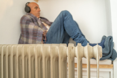 homme avec une couverture dans une maison avec un radiateur en premier plan